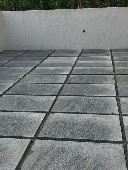 A completed patio using large, square Sadahalli stone slabs. The dark grout lines create a clean, geometric look that complements modern architecture.
