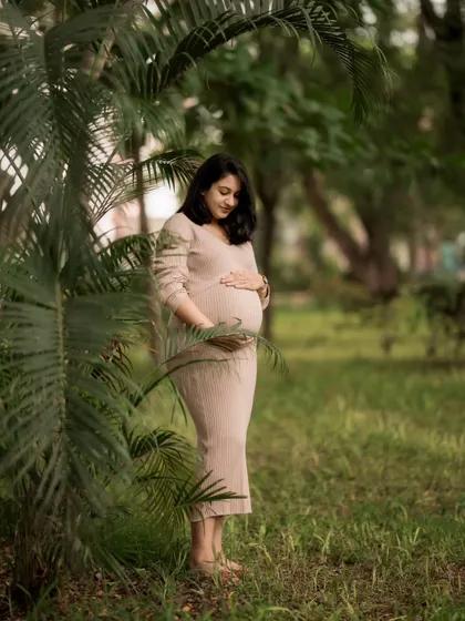 A serene solo portrait amidst lush greenery. The mother-to-be is framed by palm leaves, creating a natural and peaceful atmosphere for her maternity picture.