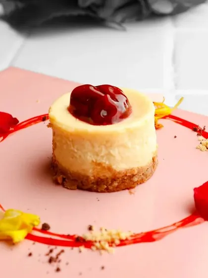 Our Baked Cherry Cheesecake, artistically plated with scattered flower petals and a swirl of berry coulis. Every dessert we serve is designed to be a feast for the eyes.