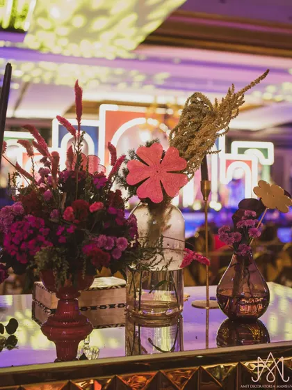A colorful floral arrangement on a bar top, with playful paper cutouts and a mix of fresh flowers and dried elements.