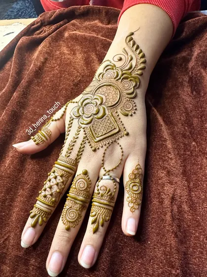 A stunning back-of-hand design with 3D flowers and jewelry-like chains. The fresh henna paste shows the intricate details before it sets.
