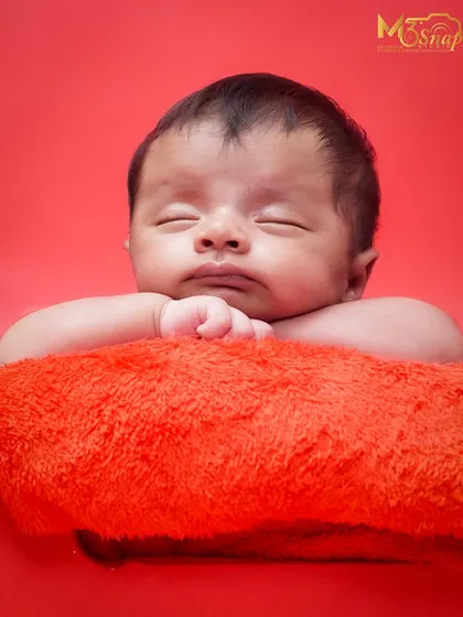 The classic "head on hands" pose against a bold red background. This pose is perfect for showing off a newborn's chubby cheeks and peaceful expression.