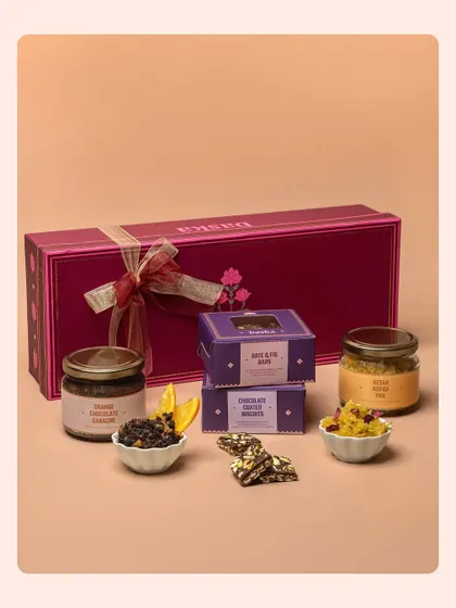 A product group shot for a Rakhi hamper, showcasing jars of dry fruits and boxes of sweets. The arrangement is designed to show the variety and value within the festive collection.