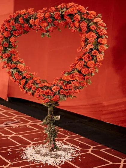 A heart-shaped floral sculpture made entirely of red-orange roses. This standalone piece is a beautiful and symbolic addition to any wedding or engagement decor.