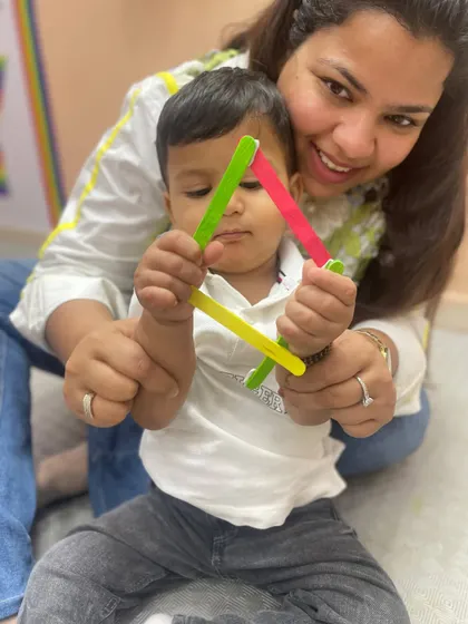 A mother and child in our Pitampura class hold up a triangle made from popsicle sticks, a fun, hands-on geometry lesson.