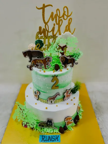 A "Two Wild" birthday cake with a forest animal theme. This two-tiered cake is decorated with various animal figures like tigers and lions, set in a lush green landscape.
