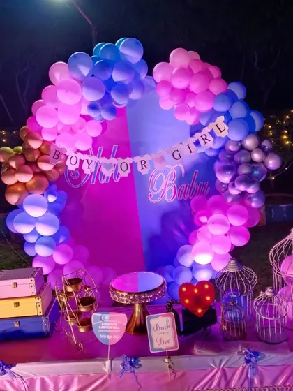 A "Boy or Girl" themed baby shower decoration. The backdrop is split between pink and blue, surrounded by a matching balloon arch, building anticipation for the big reveal.