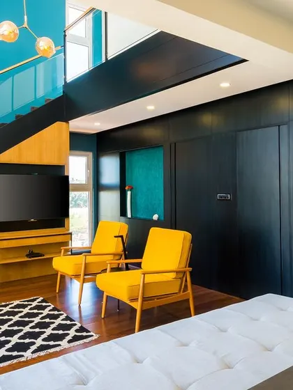 This space captures modernist principles with its clean lines, functional design, and bold color choices. The contrast between the dark walls, bright yellow chairs, and rich wood tones creates a dynamic and energetic living area.