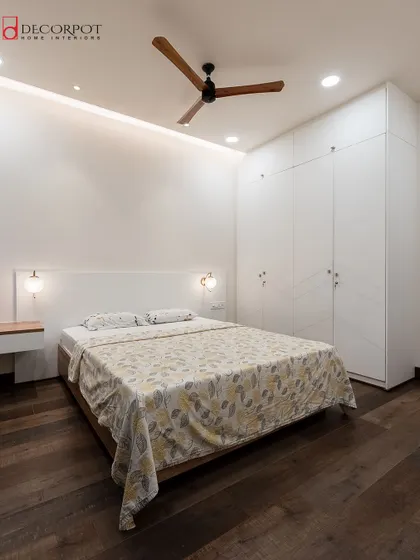 A minimalist bedroom design with clean lines and a calm, neutral palette. The floor-to-ceiling white hinged wardrobe blends seamlessly into the wall, making the room feel spacious and airy.