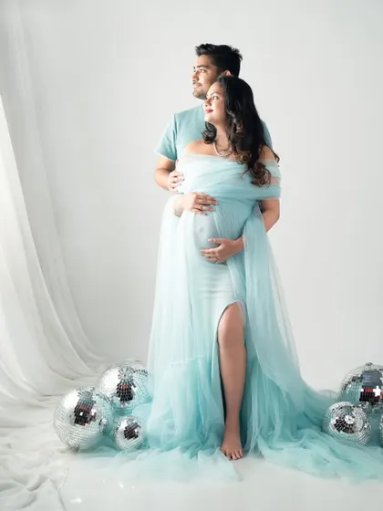 Light, airy, and beautiful. This expecting mother is glowing in a pastel blue gown, surrounded by disco balls for a fun, dreamy effect against a clean white backdrop.