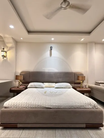 This bed showcases a minimalist aesthetic with its clean lines and simple, curved headboard. The rich brown fabric and matching wooden side tables create a cohesive and calming atmosphere.