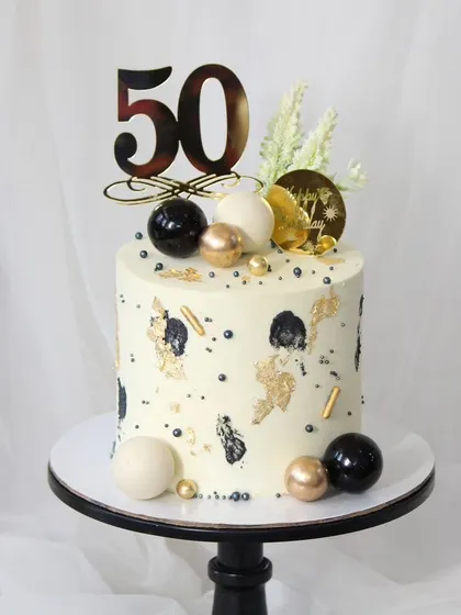 A modern and artistic cake for a 50th birthday celebration. The design features abstract black and gold brushstrokes, accented with black, white, and gold spheres for a contemporary feel.