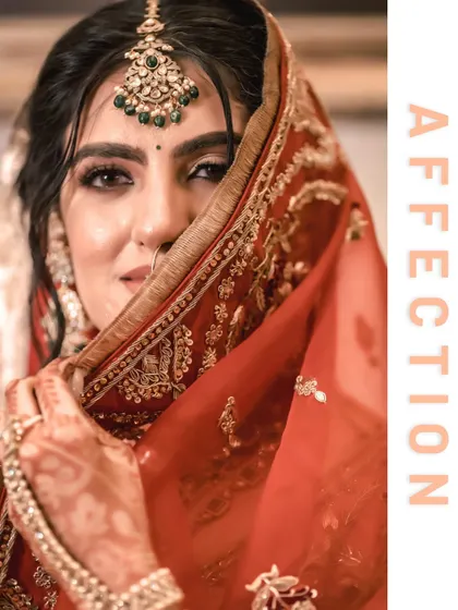 A close-up of the bride, Vanaja, peeking from behind her dupatta, her eyes full of affection and a hint of playfulness.