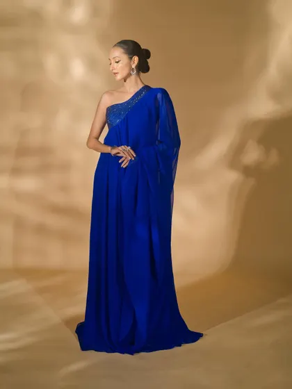 A full-length shot of a one-shoulder blue gown from Nikhil Thampi's collection. The elegant pose and soft lighting emphasize the graceful drape and flow of the fabric.