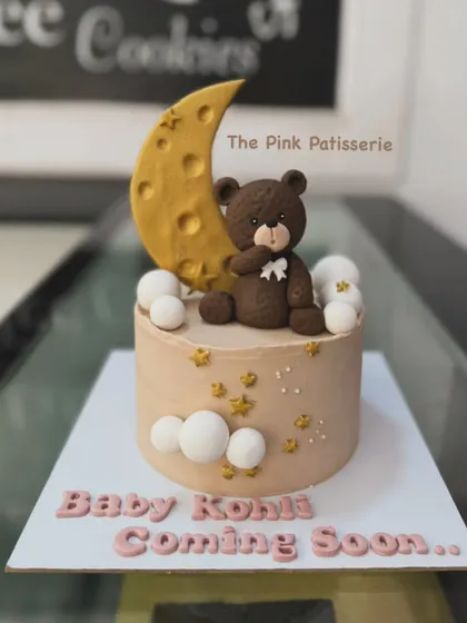 A cute baby shower cake announcing "Baby Kohli Coming Soon." The design features a fondant teddy bear sitting on a crescent moon, surrounded by fondant clouds and stars.