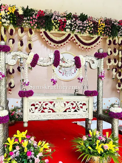 A beautifully decorated silver cradle with purple and white floral arrangements. This setup is perfect for a modern naming ceremony, combining elegance with traditional elements.