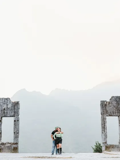 A wide shot showing the couple framed by ancient ruins against the vast mountain range, creating a sense of timelessness and adventure.