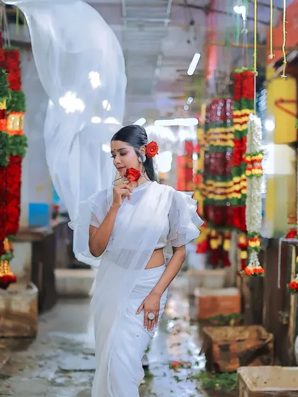 A stunning photo of a model in a modern white saree with ruffled sleeves, posing in a vibrant flower market.