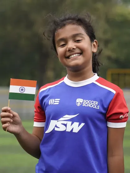 A smiling young girl holds the national flag. We believe in empowering girls through sport, building their confidence and skills.