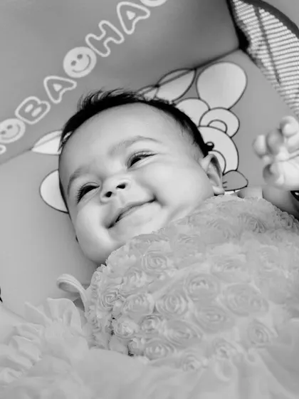 A black and white photo of a baby smiling joyfully while lying down. Monochrome photography emphasizes expression and emotion, creating a powerful and timeless image.