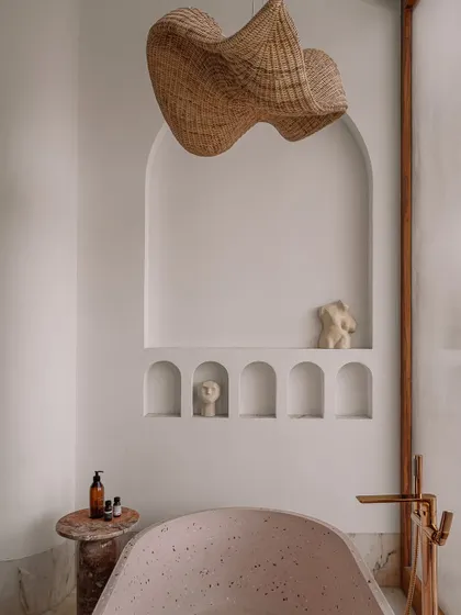 The bathtub area in the junior master ensuite, featuring a freestanding tub, a woven pendant light, and a series of arched niches for displaying art and personal items.