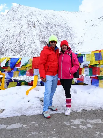 A couple from our group stands against a wall of colorful prayer flags with a snow-covered mountain in the background.