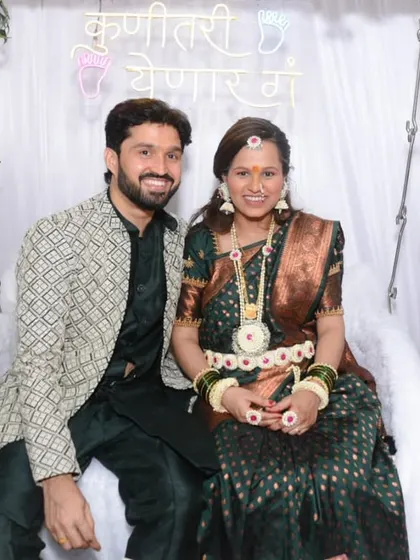 The happy couple seated together at their baby shower, posing for a classic portrait in front of the neon sign and floral decor.
