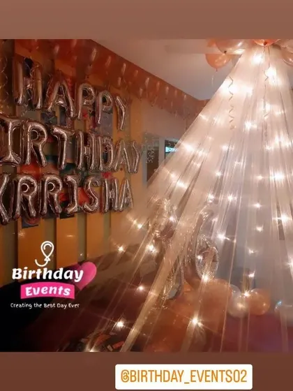 A personalized canopy decoration with "Happy Birthday Krisha" in silver foil letters against an orange wall, creating a warm and inviting look.