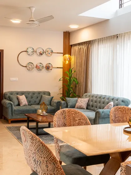 A view from the dining area into the living room, showing how the two spaces are connected yet distinct. The elegant dining chairs in the foreground complement the teal sofas in the background, creating a unified color story.