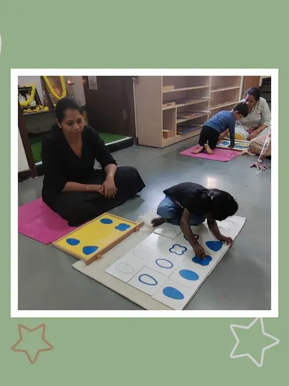 Dwiti is fully absorbed in her work with the geometric cabinet, matching shapes. Her mother watches on, seeing her daughter's ability to focus and solve problems independently.