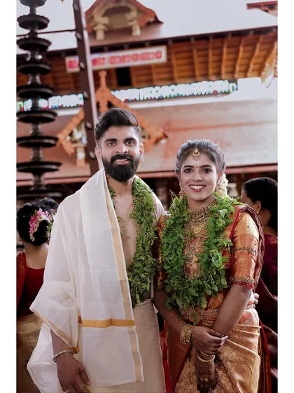 A classic portrait of a newly married couple at their temple wedding, adorned with green garlands.