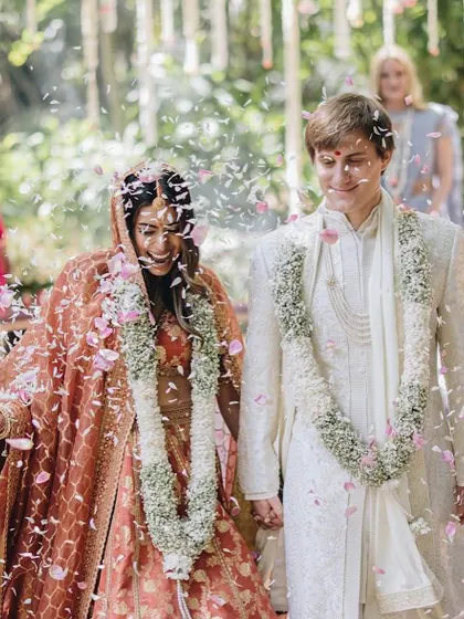 A shower of petals for the happy couple. Her rust-colored Sabyasachi lehenga and his ivory sherwani are a perfect example of modern, coordinated elegance.