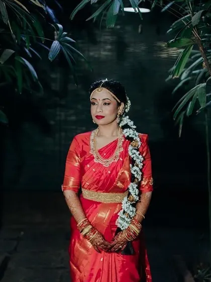 A stunning full-length portrait. The bride's makeup features a classic red lip and a traditional braid adorned with jasmine flowers, creating an iconic South Indian bridal look.