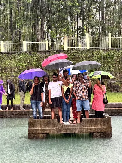 A group enjoying the rain at the Devagange temple pond, holding umbrellas.