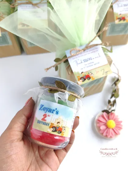 Holding the personalized layered candle from the farm-themed birthday set, showcasing the custom sticker and colorful wax layers.