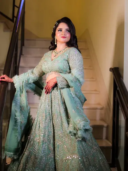 An elegant bridal portrait on a staircase. The bride's mint-green lehenga and confident pose create a look of modern royalty.