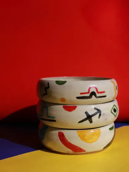 A stack of bowls from the 'Playful Mornings' collection, decorated with colorful zodiac signs and abstract shapes.