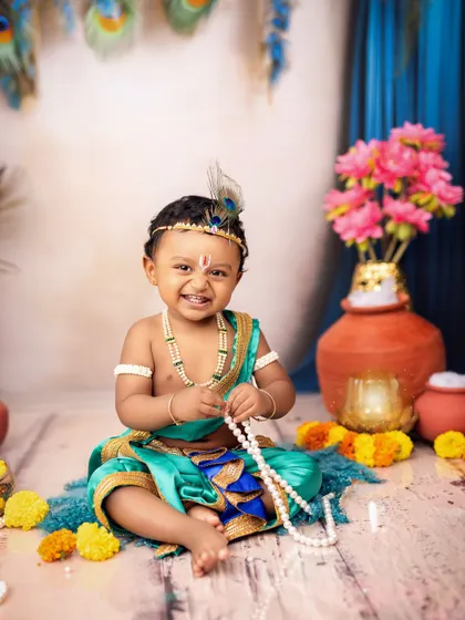 A cheeky grin from our little Krishna, who is playing with a string of pearls. His personality shines through in this adorable shot.