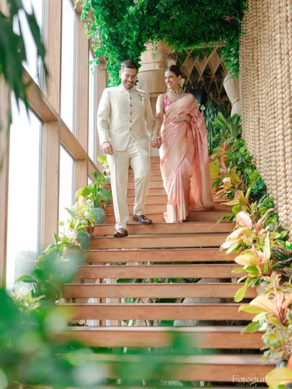 An elegant shot of the couple descending a plant-lined wooden staircase, hand-in-hand, during their engagement ceremony.