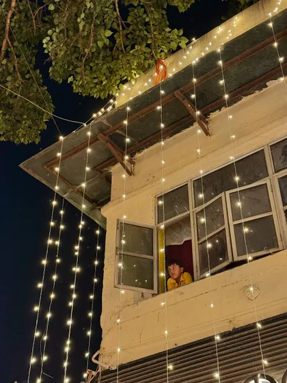 A child looking out of a window decorated with fairy lights. A moment of pure, simple joy and wonder that is so characteristic of festival time.