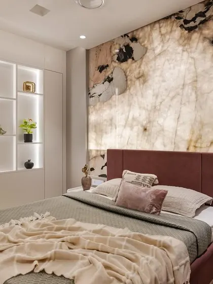 This master bedroom features a stunning backlit Pink Flower Lava Quartzite marble wall. This solution corrected slanted walls to align with Vaastu principles and created a luminous, luxurious effect.