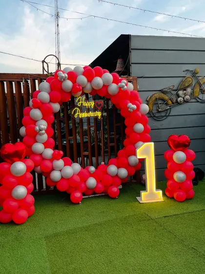 A closer look at the red and silver themed first-anniversary rooftop decor. The circular balloon arch and marquee number create a bold and festive look.