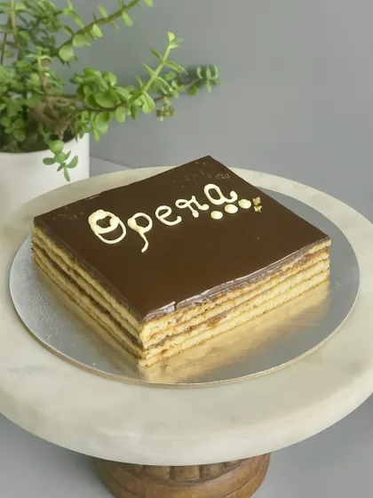 The classic French Opera cake is a masterpiece of precision. It has thin layers of almond sponge soaked in coffee syrup, layered with coffee buttercream and chocolate ganache, and topped with a chocolate glaze. Elegant, rich, and timeless.