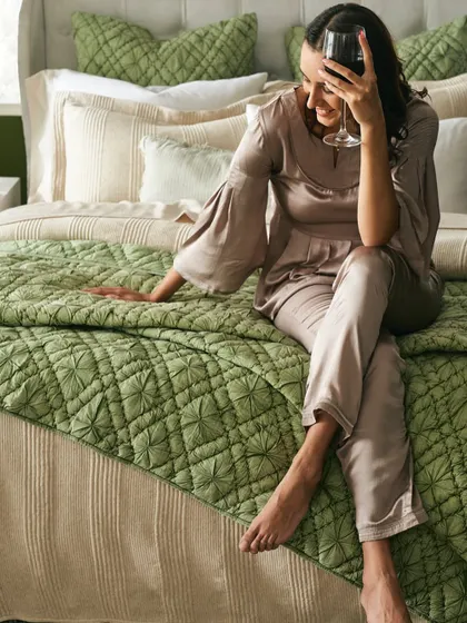 A lifestyle image that associates the product with relaxation and personal indulgence. The warm lighting and relaxed pose create a mood of sophisticated comfort for this bedding campaign.