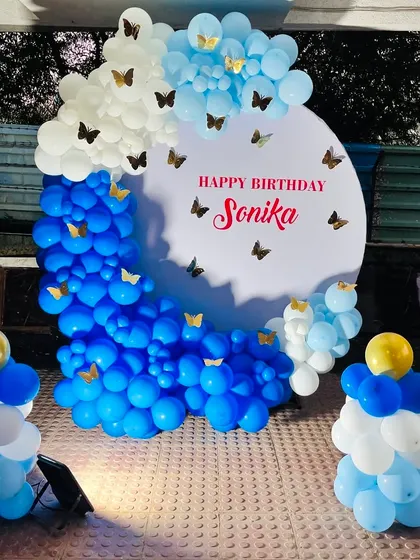 A simple and elegant outdoor setup with a blue and white balloon arch decorated with butterflies, perfect for a daytime party.
