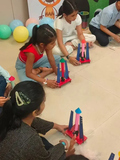 A group of kids sitting on the floor, each assembling their own colorful rocket. We provide all the pre-cut parts and decorations for personalization.