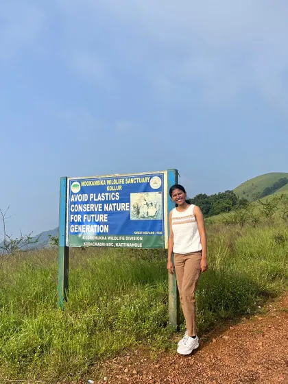 A trekker stands by a sign for the Mookambika Wildlife Sanctuary, reminding us to conserve nature.