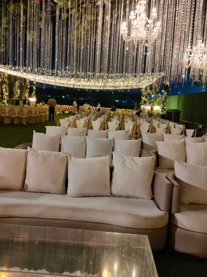 An elegant lounge seating arrangement under a sky of hanging crystals and chandeliers. The neutral-toned sofas and clear acrylic tables create a sophisticated space for guests to mingle.