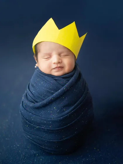 A little king in the making. This newborn is wrapped snugly in a starry blue swaddle, dreaming royally. The simple paper crown adds a playful and adorable touch.