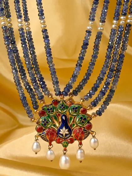 The full view of the Rajasthani peacock pendant, set on five lines of sapphire cut-beads interspersed with pearls. This shows the piece as a complete, wearable work of art, blending gemology with traditional craftsmanship.
